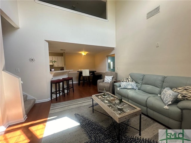 living room featuring visible vents, a high ceiling, wood finished floors, baseboards, and stairs