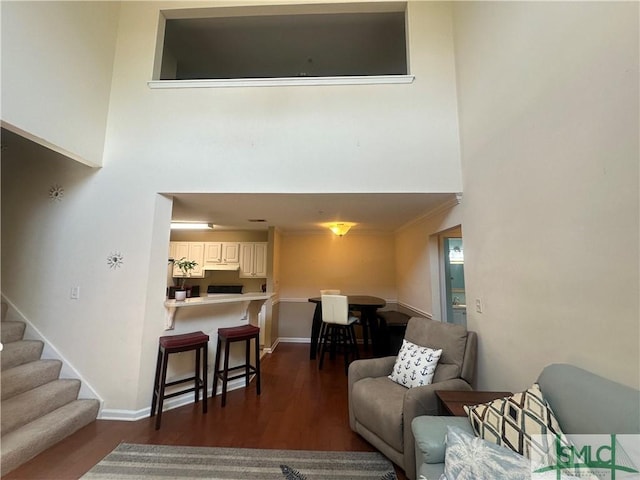 living area with dark wood-style floors, baseboards, a high ceiling, and stairs