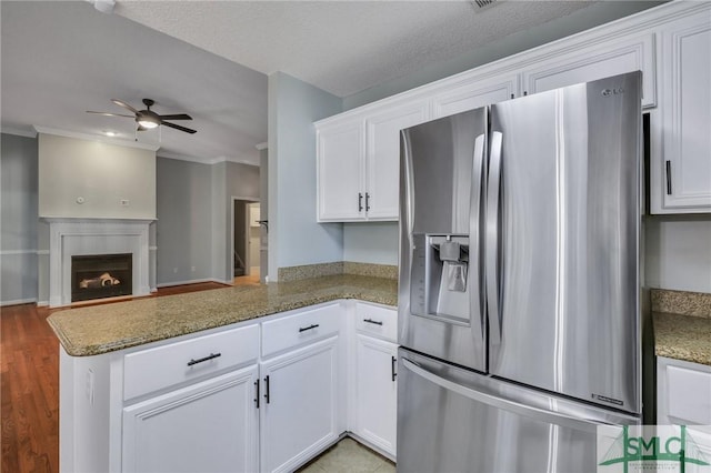 kitchen with kitchen peninsula, stainless steel fridge, white cabinets, and dark stone counters