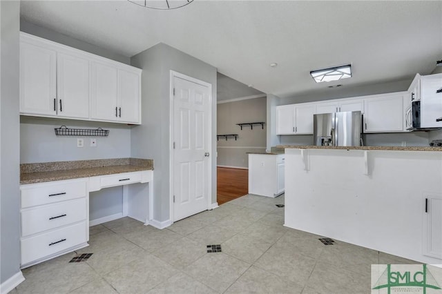 kitchen with white cabinetry, stainless steel fridge, a kitchen bar, and light tile patterned flooring