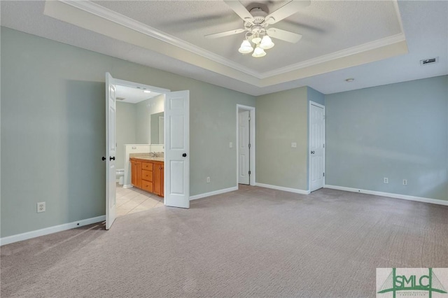 unfurnished bedroom with crown molding, ceiling fan, connected bathroom, a tray ceiling, and light colored carpet