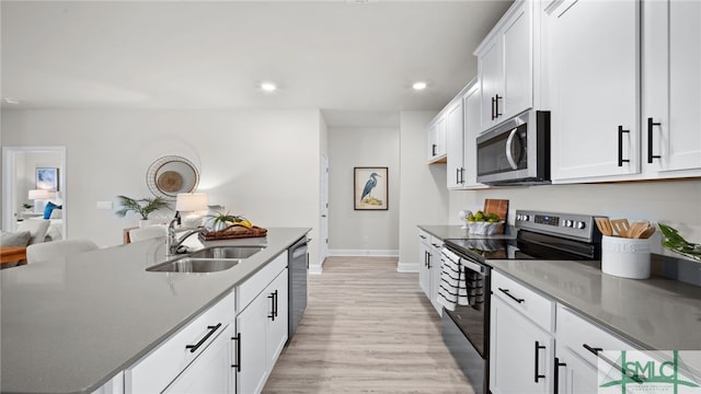 kitchen featuring white cabinets, stainless steel appliances, dark stone counters, sink, and light hardwood / wood-style flooring