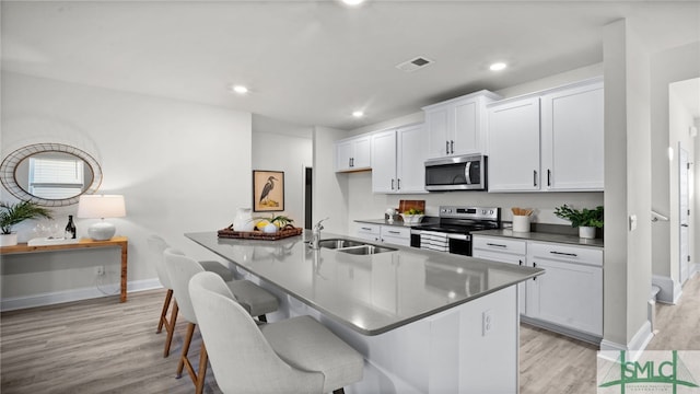 kitchen featuring light hardwood / wood-style flooring, appliances with stainless steel finishes, sink, white cabinets, and a kitchen bar