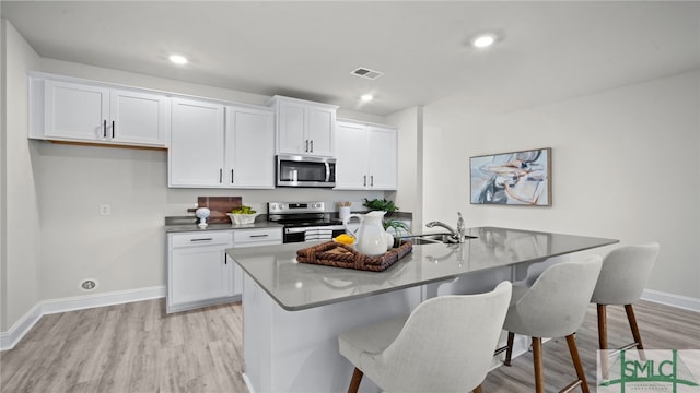 kitchen featuring white cabinets, stainless steel appliances, a breakfast bar area, and light hardwood / wood-style floors