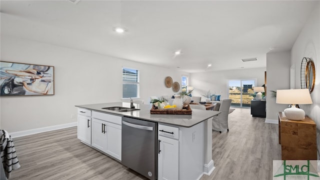 kitchen featuring stainless steel dishwasher, white cabinets, light wood-type flooring, sink, and an island with sink