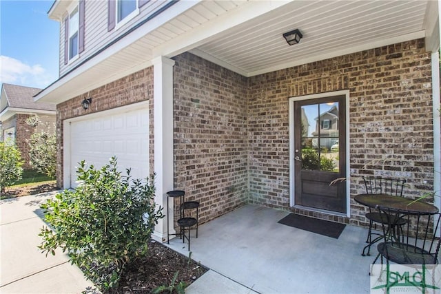 view of exterior entry featuring a garage, brick siding, and a patio area