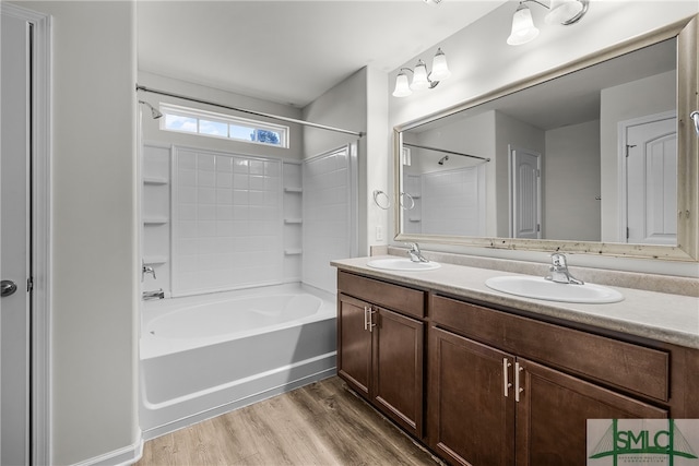 bathroom featuring double vanity, shower / bathtub combination, a sink, and wood finished floors