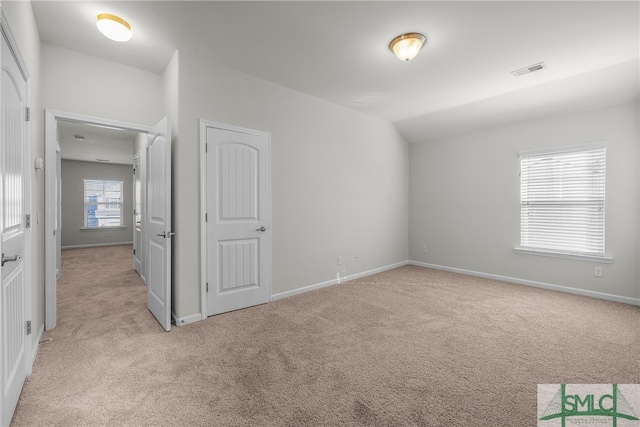 spare room featuring lofted ceiling, baseboards, visible vents, and light colored carpet