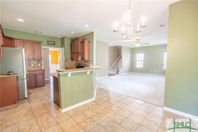 kitchen with hanging light fixtures, tasteful backsplash, kitchen peninsula, light colored carpet, and refrigerator