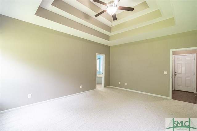 carpeted empty room featuring baseboards, a raised ceiling, and a ceiling fan