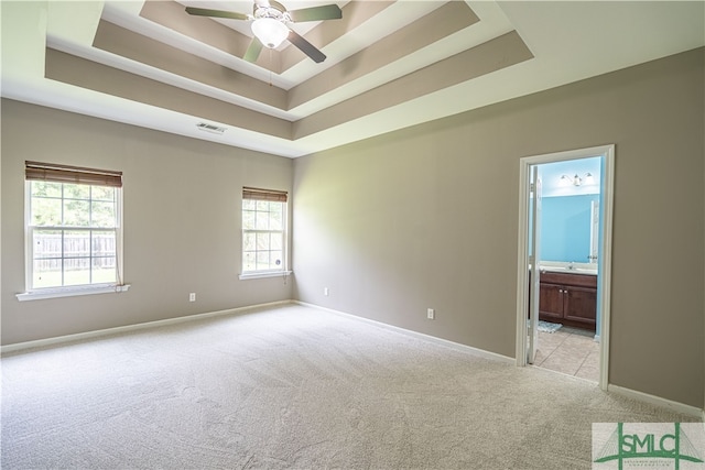 empty room featuring ceiling fan, light carpet, and a raised ceiling