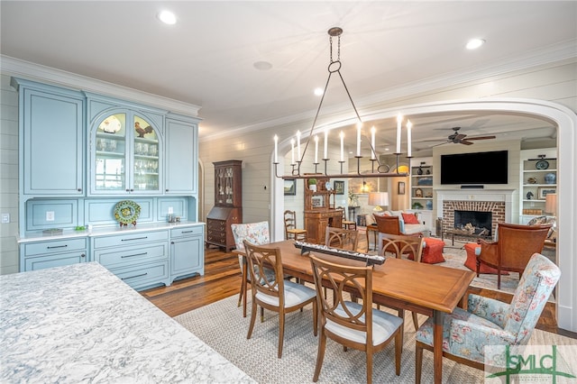 dining room featuring ornamental molding, a brick fireplace, hardwood / wood-style flooring, and ceiling fan