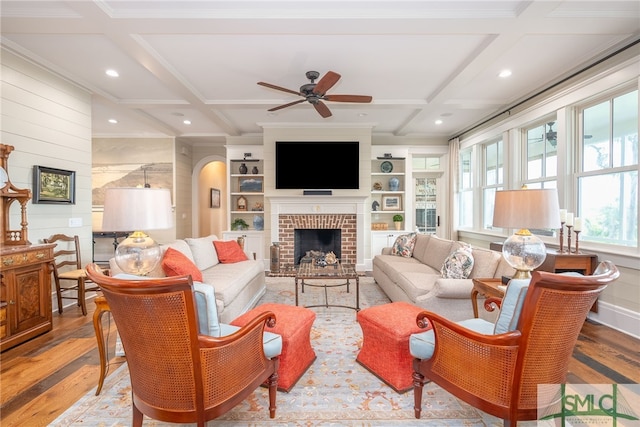 living room featuring ceiling fan, coffered ceiling, light wood-type flooring, and a brick fireplace