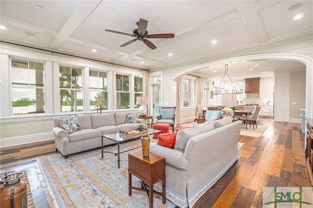 living room with wood-type flooring, ceiling fan with notable chandelier, coffered ceiling, beamed ceiling, and crown molding