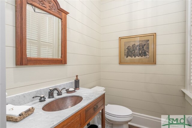 bathroom featuring toilet, wood walls, and vanity