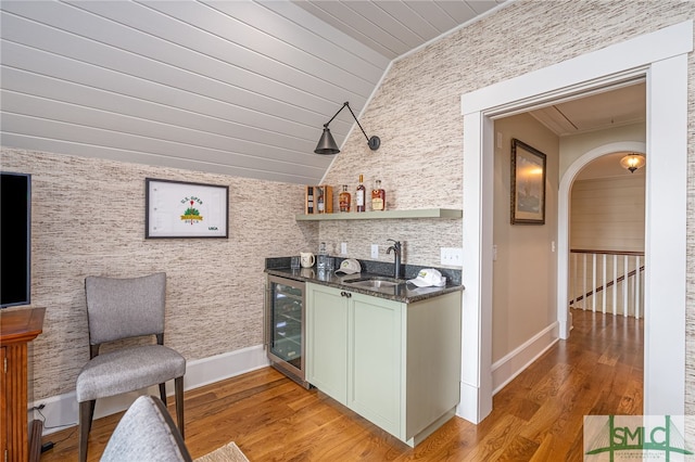 bar with lofted ceiling, wine cooler, light hardwood / wood-style flooring, sink, and green cabinetry