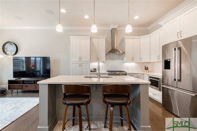 kitchen with appliances with stainless steel finishes, sink, wall chimney exhaust hood, dark wood-type flooring, and a center island with sink