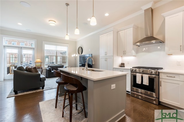 kitchen featuring stainless steel gas stove, wall chimney exhaust hood, ornamental molding, dark wood-type flooring, and white cabinets