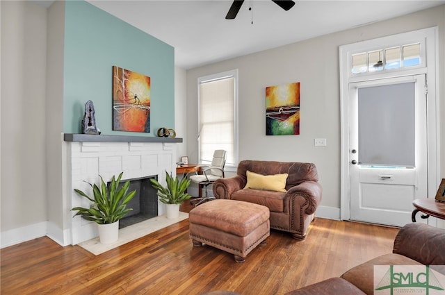 living room featuring ceiling fan, wood-type flooring, and a brick fireplace