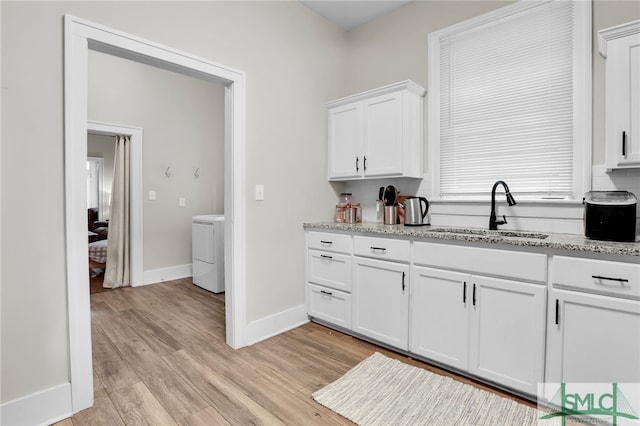 kitchen with light stone countertops, light wood-type flooring, sink, white cabinets, and washer / clothes dryer