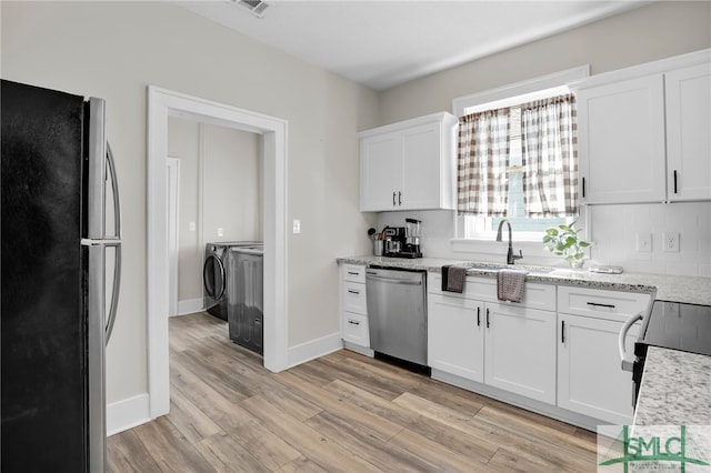 kitchen featuring light stone countertops, stainless steel appliances, separate washer and dryer, light hardwood / wood-style floors, and white cabinetry