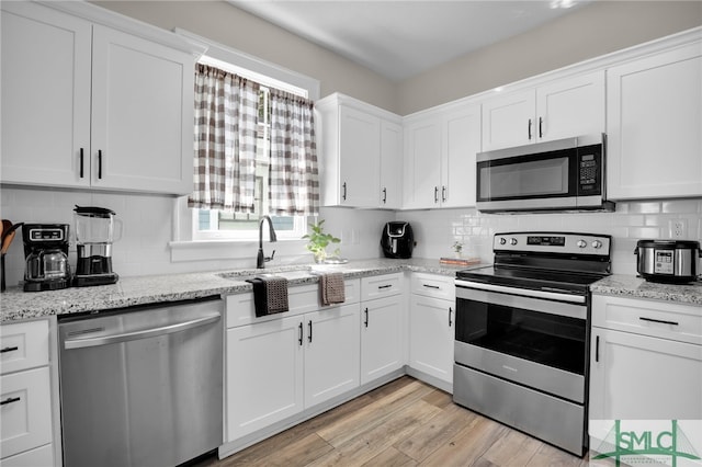 kitchen with decorative backsplash, white cabinets, light wood-type flooring, and appliances with stainless steel finishes