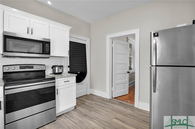 kitchen with white cabinets, backsplash, light wood-type flooring, and stainless steel appliances