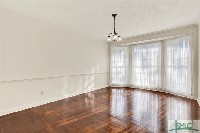 empty room with a textured ceiling, an inviting chandelier, dark hardwood / wood-style floors, and ornamental molding