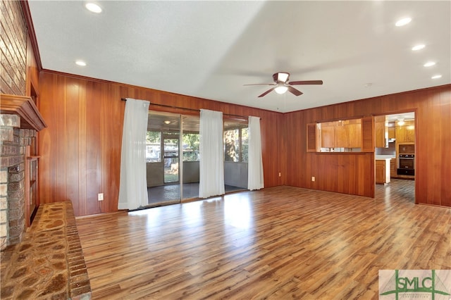 unfurnished living room featuring ceiling fan, hardwood / wood-style flooring, crown molding, and wood walls