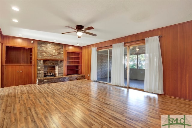 unfurnished living room featuring light hardwood / wood-style flooring, wooden walls, a brick fireplace, and built in shelves