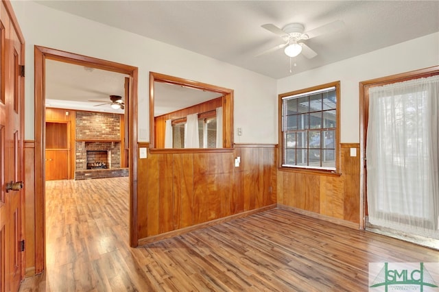 interior space featuring ceiling fan, wood walls, wood-type flooring, and a brick fireplace