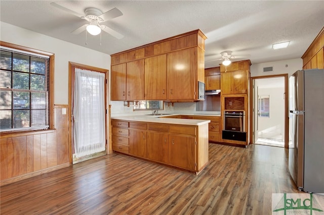 kitchen featuring dark hardwood / wood-style flooring, a textured ceiling, stainless steel refrigerator, wall oven, and wooden walls