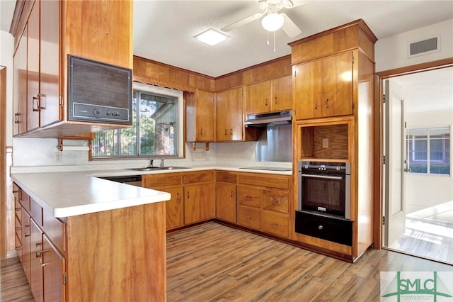 kitchen featuring stainless steel oven, light hardwood / wood-style flooring, kitchen peninsula, backsplash, and sink