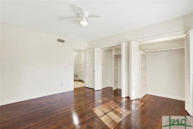 unfurnished bedroom with dark wood-type flooring, ceiling fan, and two closets