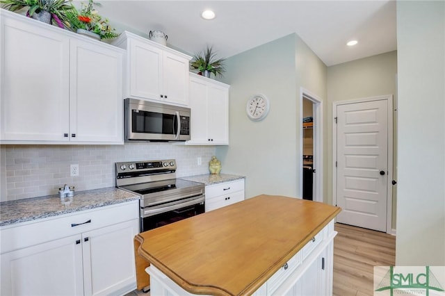 kitchen featuring stainless steel appliances, white cabinetry, light wood-style flooring, and tasteful backsplash