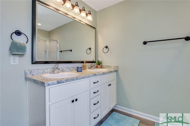 full bath featuring double vanity, a shower stall, baseboards, and a sink