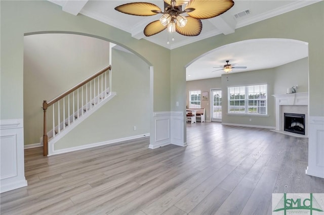 unfurnished living room featuring crown molding, visible vents, light wood-style flooring, ceiling fan, and stairs