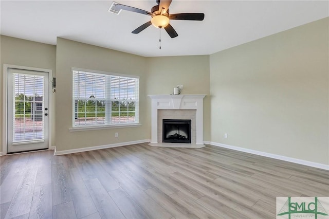 unfurnished living room with a fireplace with flush hearth, ceiling fan, light wood-style flooring, and baseboards