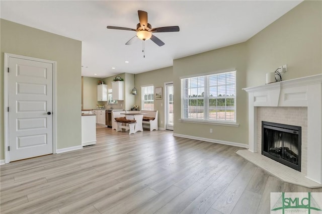 living room featuring baseboards, light wood-style flooring, ceiling fan, a fireplace, and recessed lighting