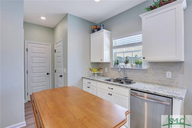 kitchen featuring tasteful backsplash, light wood-style flooring, stainless steel dishwasher, white cabinets, and a sink