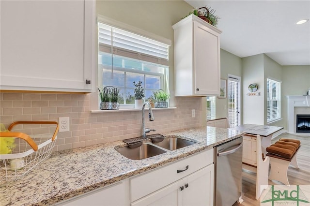 kitchen featuring dishwasher, a fireplace, a sink, and white cabinetry