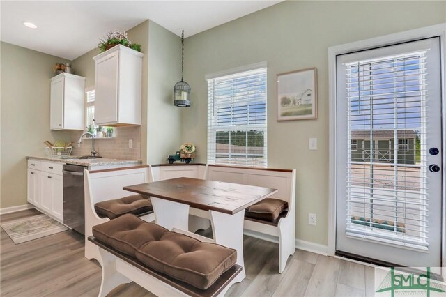 kitchen featuring a sink, white cabinetry, stainless steel dishwasher, light wood-type flooring, and decorative backsplash