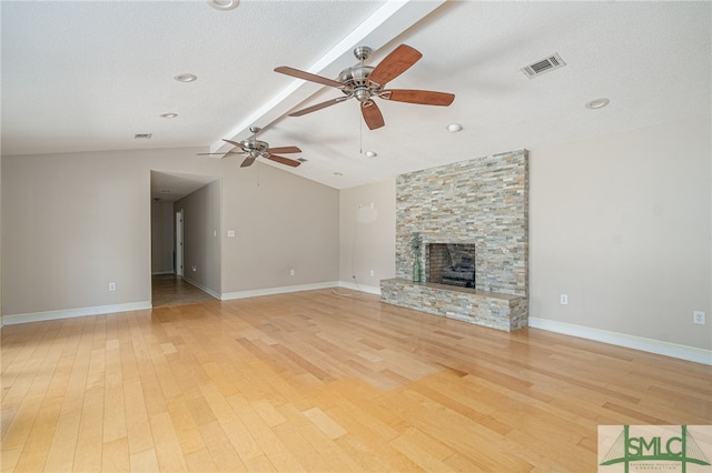 unfurnished living room with a stone fireplace, vaulted ceiling with beams, ceiling fan, light hardwood / wood-style floors, and a textured ceiling