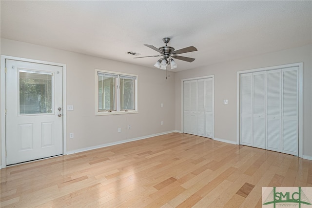 unfurnished bedroom featuring ceiling fan, two closets, a textured ceiling, and light wood-type flooring