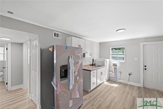 kitchen with light wood-type flooring, butcher block countertops, stainless steel refrigerator with ice dispenser, white cabinets, and sink