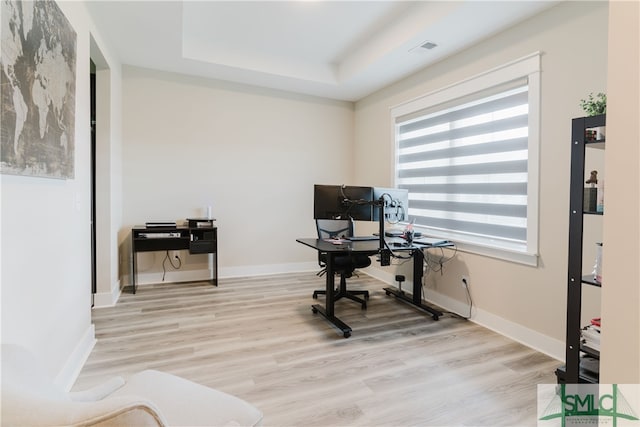 home office with a tray ceiling and light hardwood / wood-style floors