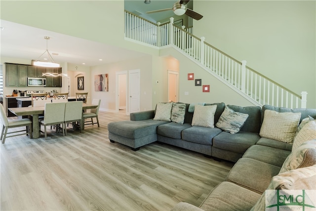 living room featuring light hardwood / wood-style floors, a towering ceiling, and ceiling fan