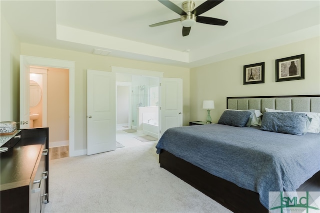 bedroom with ceiling fan, a raised ceiling, connected bathroom, and light carpet