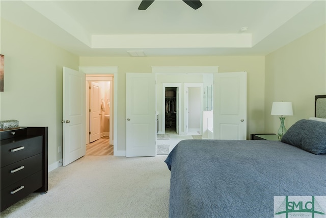 bedroom with ceiling fan, light carpet, and a tray ceiling