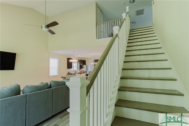 staircase featuring hardwood / wood-style flooring, a towering ceiling, and ceiling fan